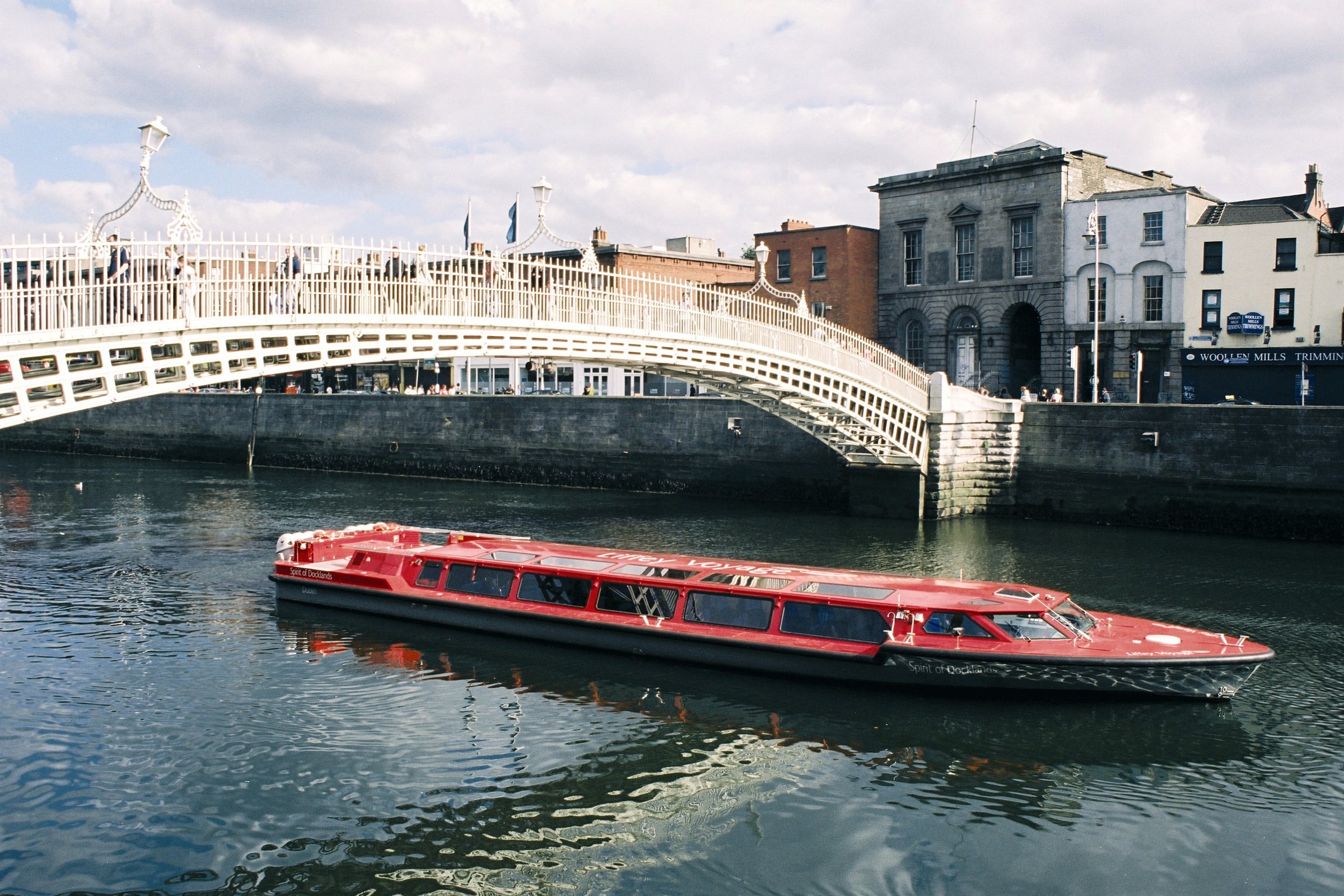 Red boat on river under ornate white bridge with buildings in background.