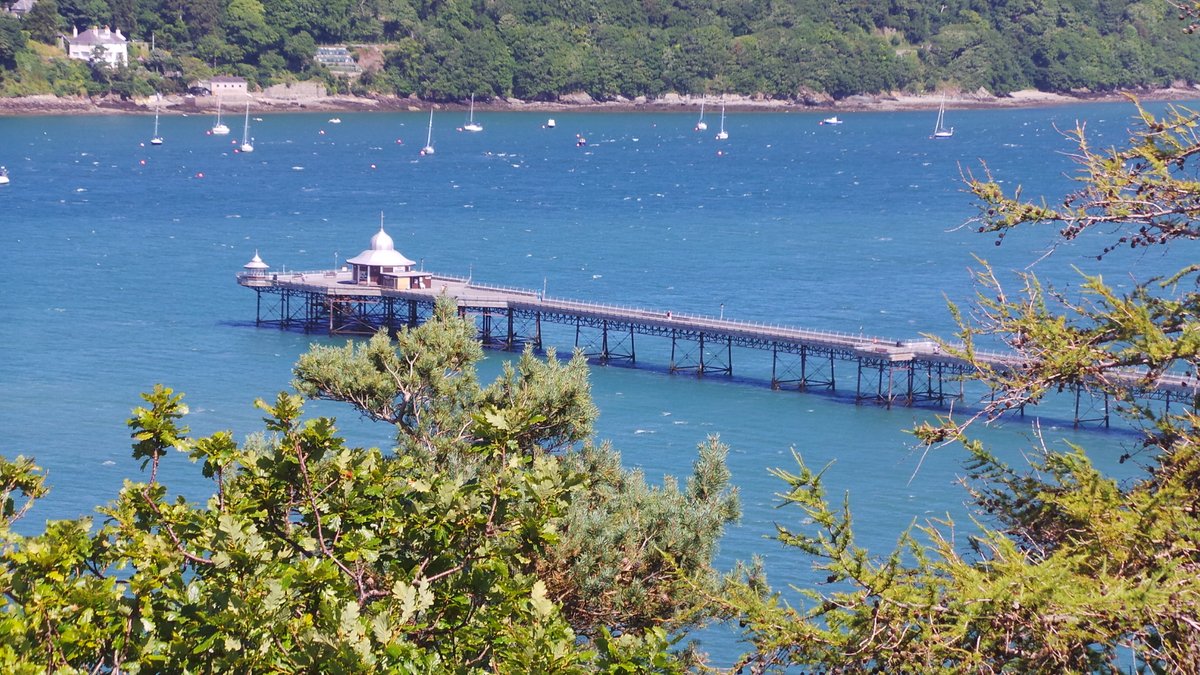A panoramic aerial view of Bangor city, Wales, showing the compact city center, Garth Pier reaching into the Menai Strait, and the mountains of Snowdonia in the background.