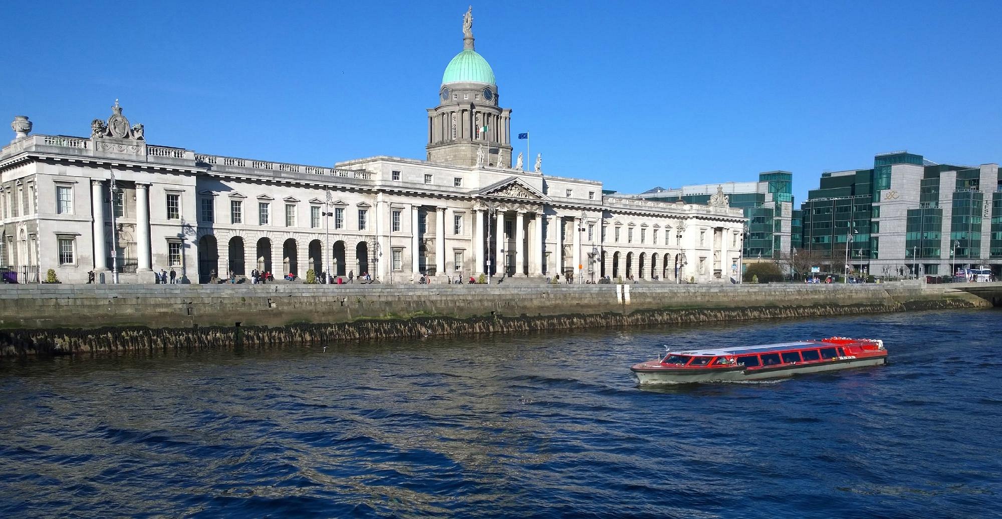 Historic building with a green dome by a river, boat passing in front.