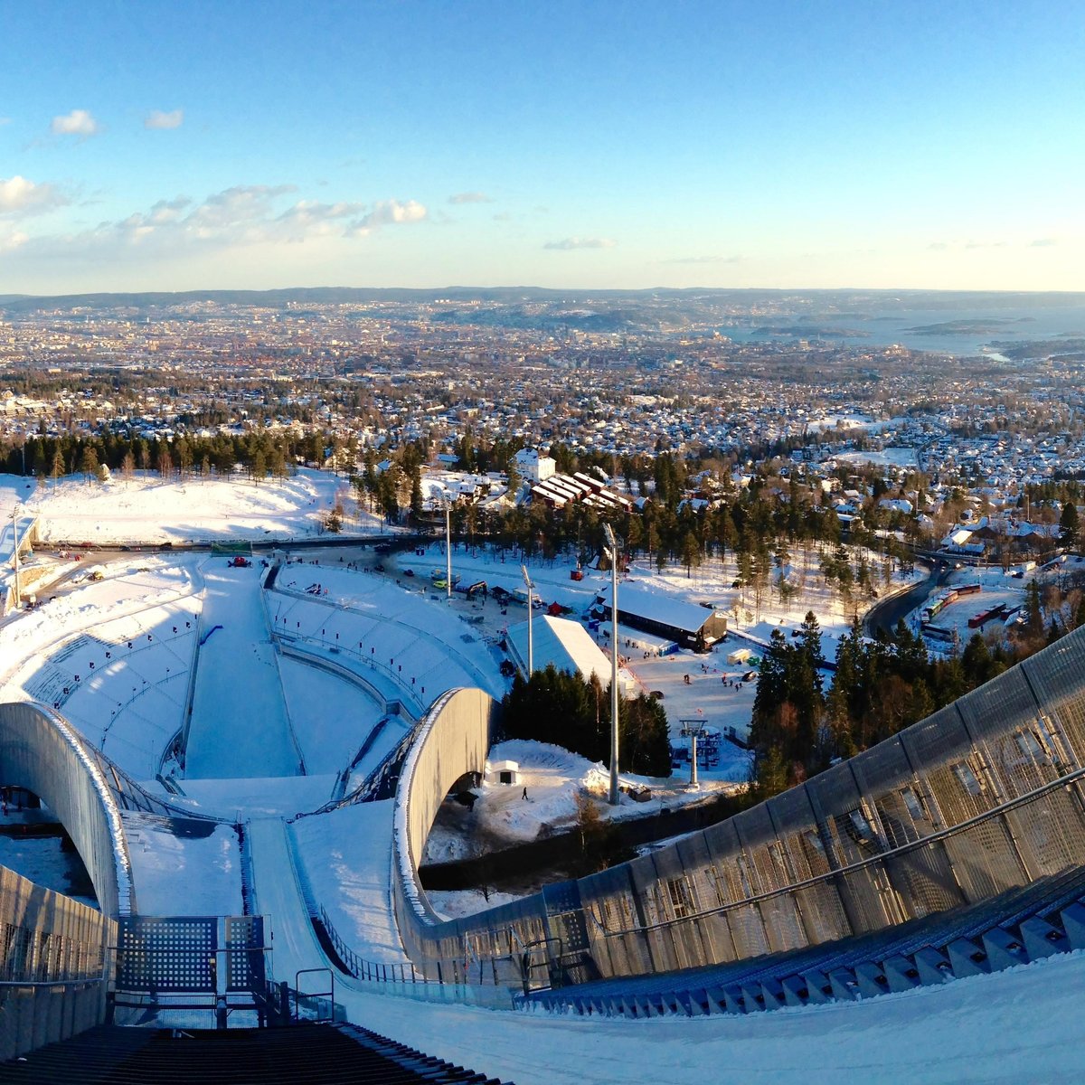 The iconic Holmenkollen Ski Jump tower, a modern steel structure, overlooking a wide panoramic view of Oslo city and the Oslo Fjord on a clear day.