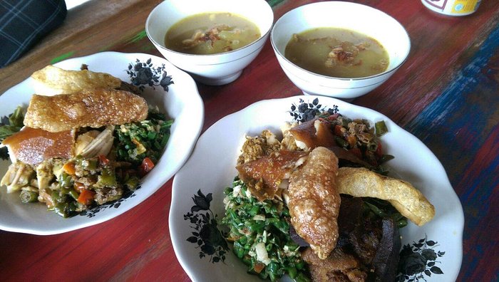 Traditional Balinese meal of Babi Guling served in white bowls with crispy pork skin, vegetables, and lawar, accompanied by soup in separate bowls on a wooden table.