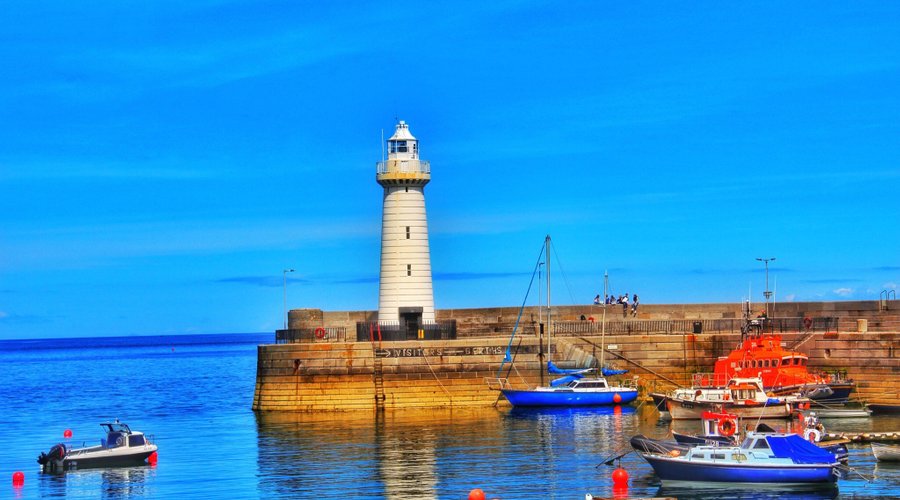 Donaghadee harbour filled with a variety of fishing and leisure boats, with colourful buildings lining the quayside under a bright sky, Northern Ireland.