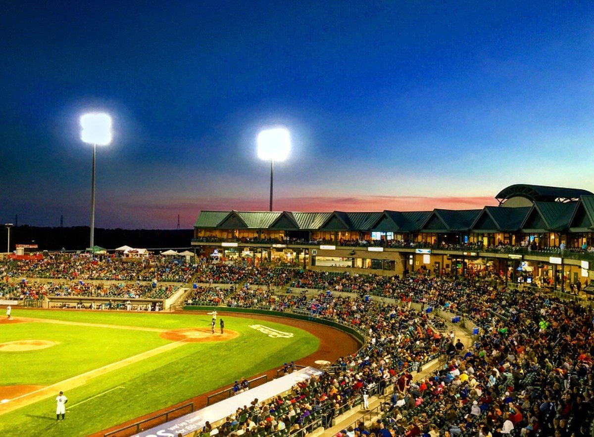 Evening view of a crowded baseball stadium during a game at TD Bank Ballpark, illuminated under the bright lights from tall light posts. The stands are packed with spectators, and the field shows players in position.