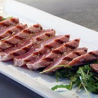 Tagliatta de atún con jugo de limón, aceite de olivo y pimienta, servida sobre una cama de arúgu
