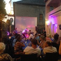 Bar/Tabac on right. Live music evening. Sport screen behind band.