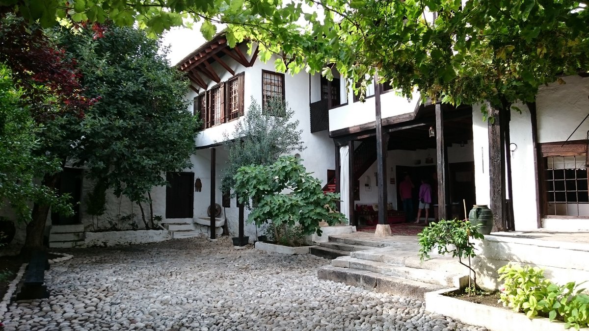 Interior courtyard of the Kajtaz House in Mostar, featuring traditional Ottoman architecture, a stone fountain, and lush greenery.