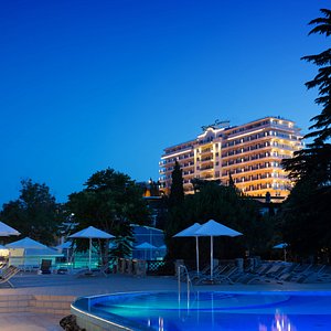 Открытый подогреваемый бассейн на фоне живописного реликтового парка и корпуса Модерн отеля Riviera Sunrise Resort & SPA.
