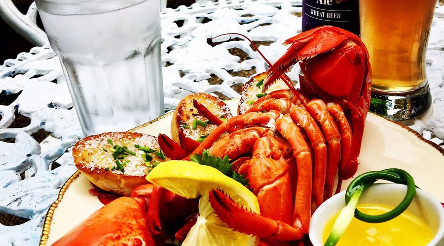 Acadian-style lobster served with garlic butter, garlic bread, lemon, and a cold beer.