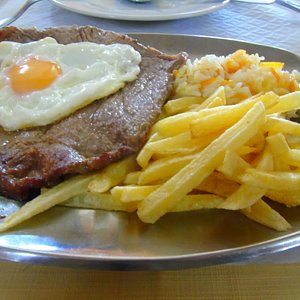 O magnífico bife à Clarinha, com ovo, o saboroso arroz, as batatas fritas estaladiças e a salada de tomate e pepino.