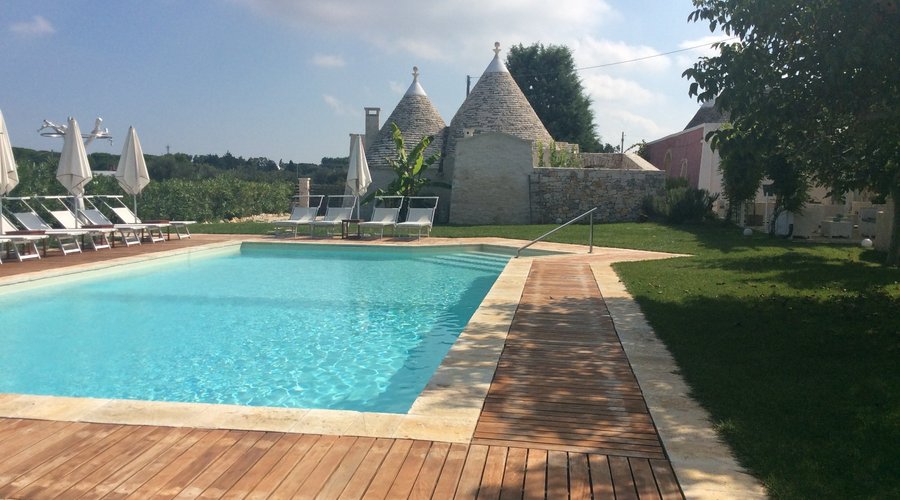 Dalla piscina, immersa nelle piante da frutta si vede uno dei trulli in cui si può soggiornare