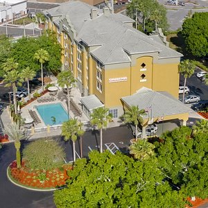 Aerial Picture Of Hotel - Parking for guests and groups with busses, covered parking at entrance for loading and unloading of vehicles, lush landscaping, and an inviting swimming pool await you.