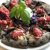 Pizza gourmet, impasto al carbone vegetale con tartare di scottona, cappuccio viola, burrata e scaglie di grana.