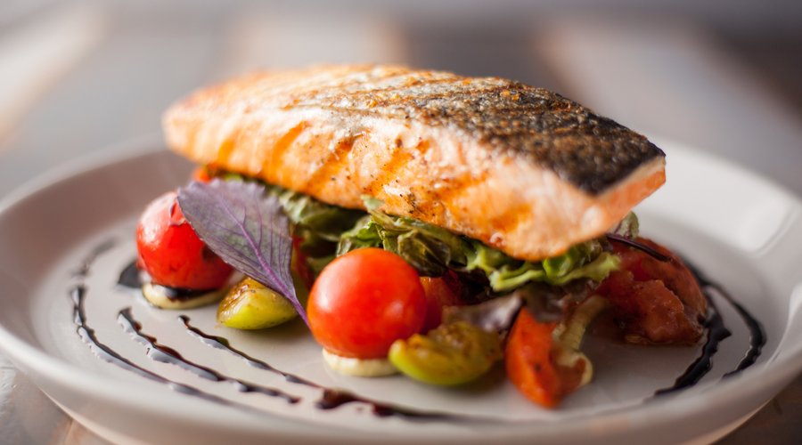 Salmón al grill sobre una cama de tomates asados acompañado de mx de lechugas y salsa pesto. 