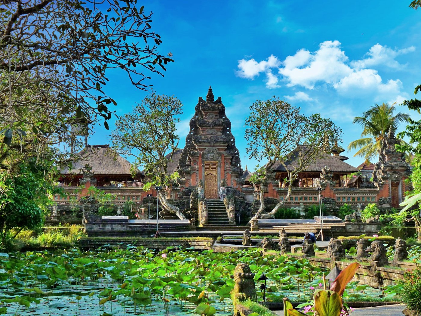 Beautiful Hindu temple with pink lotus flowers in foreground and traditional Balinese architecture