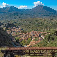 Sulla sinistra la Rocca dell'Armo, luogo storico e paesaggistico, dove è ubicato il Castello Ruggero. In primo piano il ponte in ferro della Ferrovia Calabro-Lucana, vincolato dal MiBACT