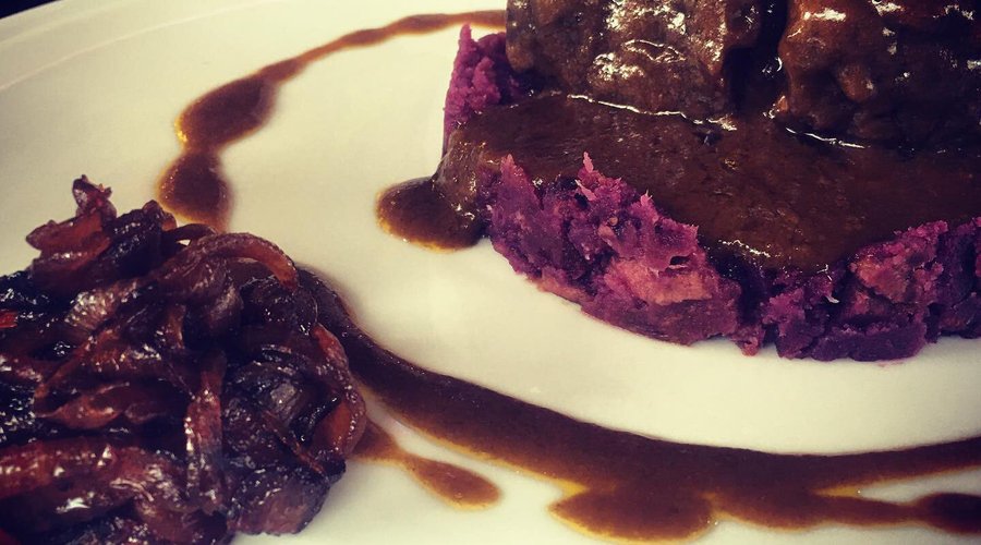 Guancia di manzo brasata al vino rosso, su purè di patate viola, nappata con la sua salsa ed accompagnata con cipolle caramellate