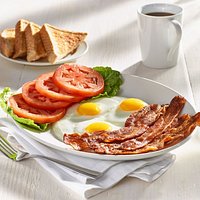 Five strips of thick bacon, three eggs, and freshly sliced tomatoes served with thick toast.