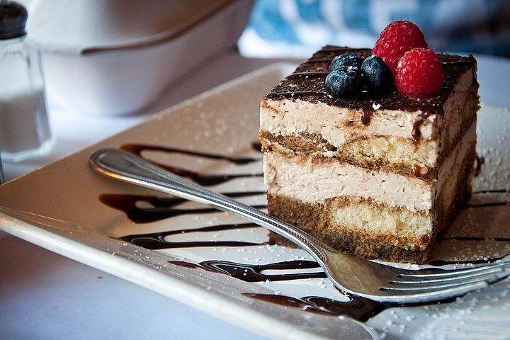 A single square of tiramisu on a plate drizzled with chocolate.