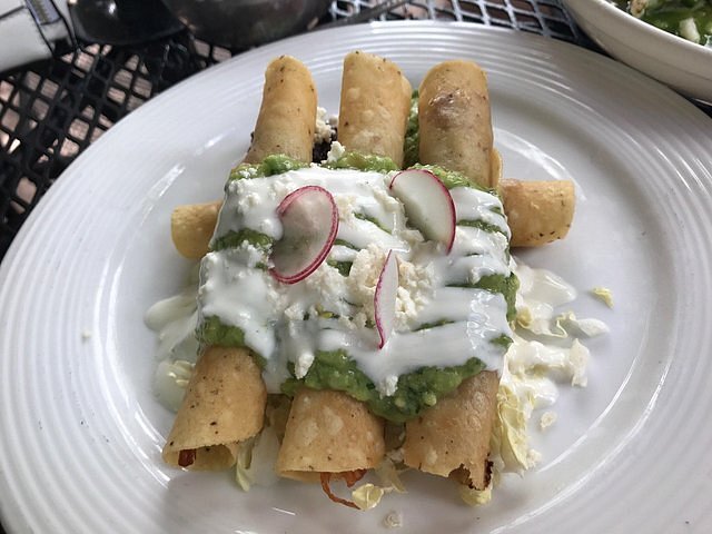 Dish with taquitos covered in crema and green sauce.