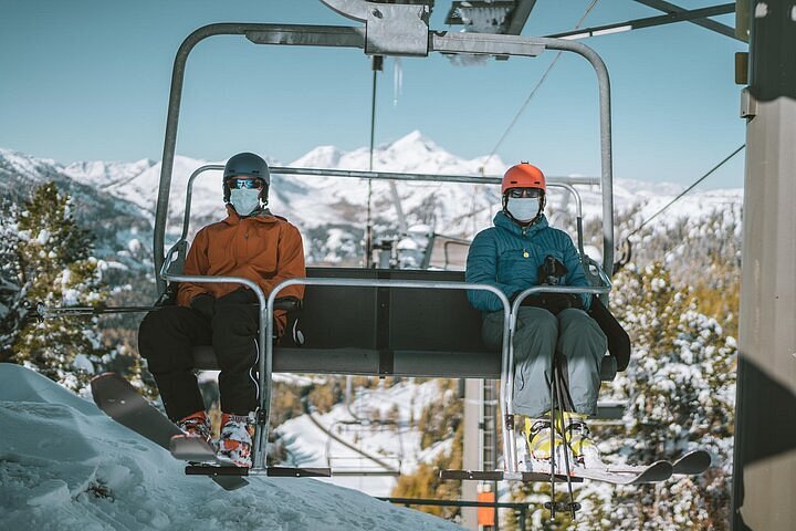 Two masked people riding a ski lift.