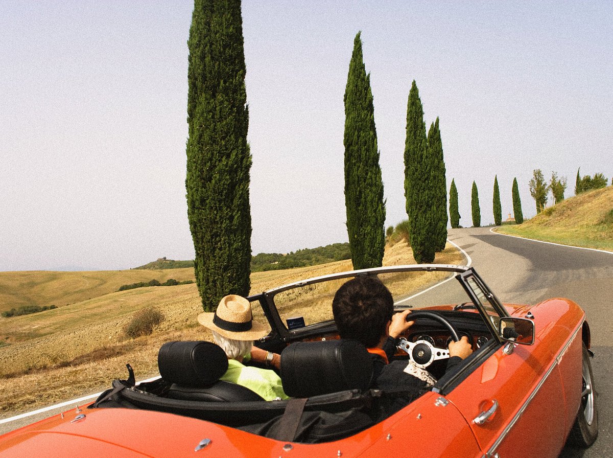 Два путешественника едут по Тоскане в красном кабриолете 