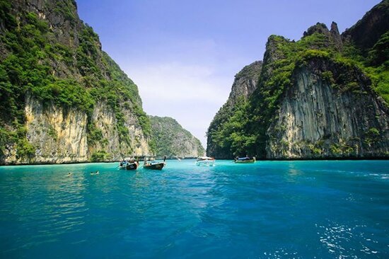 Long-tail boats floating on the crystal-clear turquoise waters between limestone cliffs at Phi Phi Islands, Thailand, captured by JKV Travel during a tropical island-hopping tour.