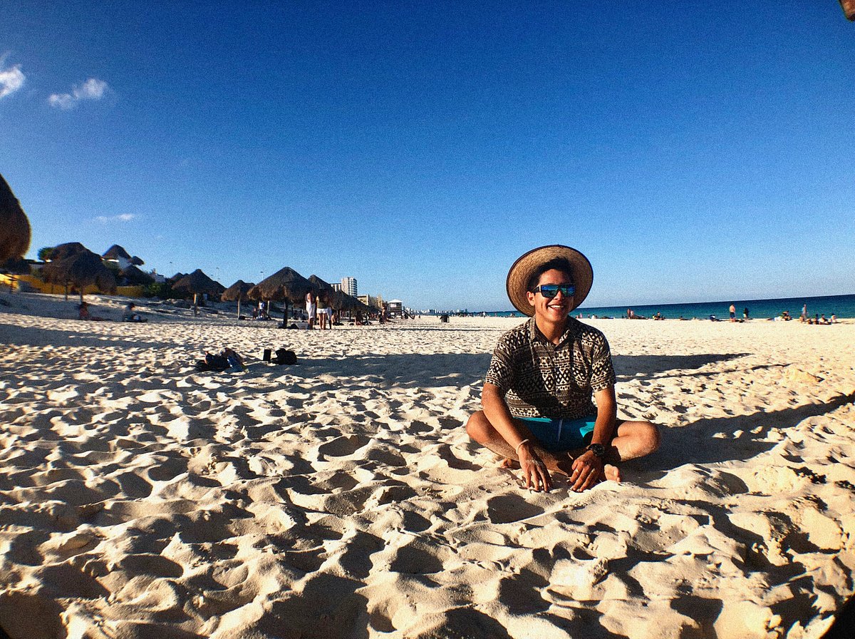 Man in a hat and sunglasses sitting on a beach in Cancun