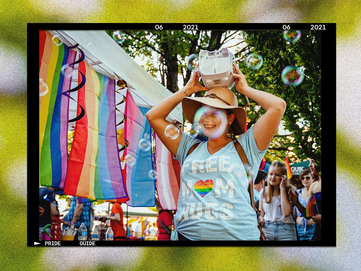 Photo of woman holding a bubble machine on her head, standing near pride flags