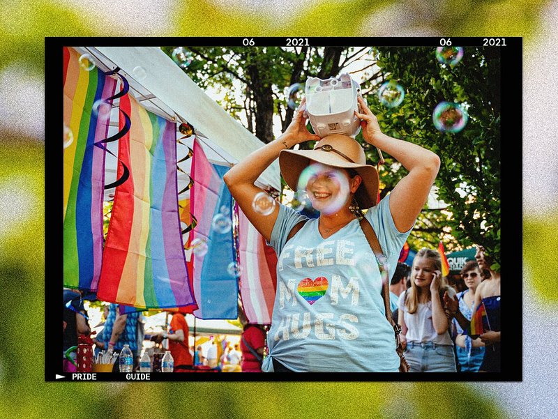 Photo of woman holding a bubble machine on her head, standing near pride flags