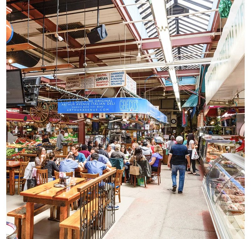 People eating at tables and vendor stalls at Arthur Avenue Market