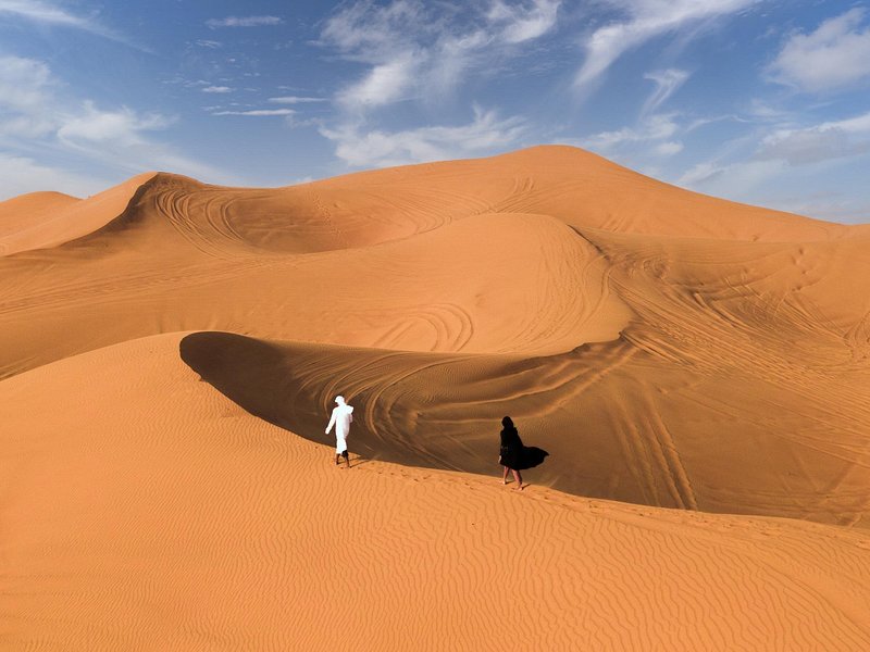 두바이의 모래 언덕 위를 걷는 두 사람