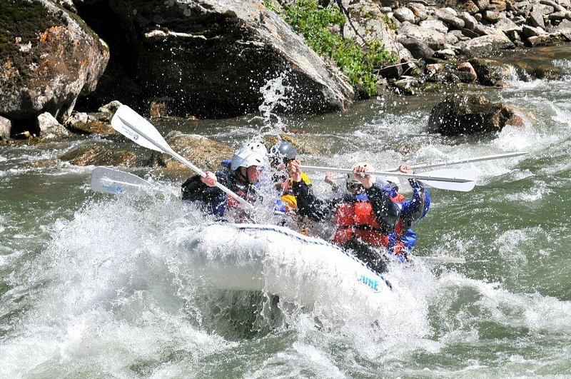 A group of people are splashed by white water on a river rafting excursion.