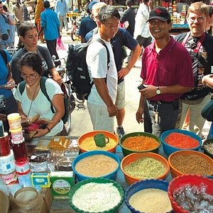 A street bazaar selling fruits and lots of spices. Two customers are emiling at the camera.