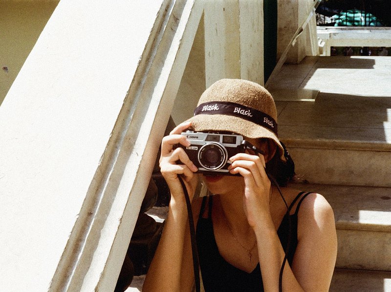 woman in hat taking a picture on a film camera