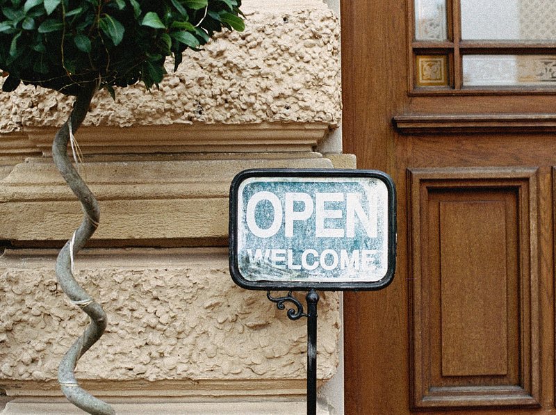 A small sign that says open welcome in front of a wall and door