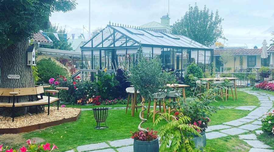 Trädgården med växthuset i bakgrunden.I växthuset kan man sitta upp till 20 personer . 