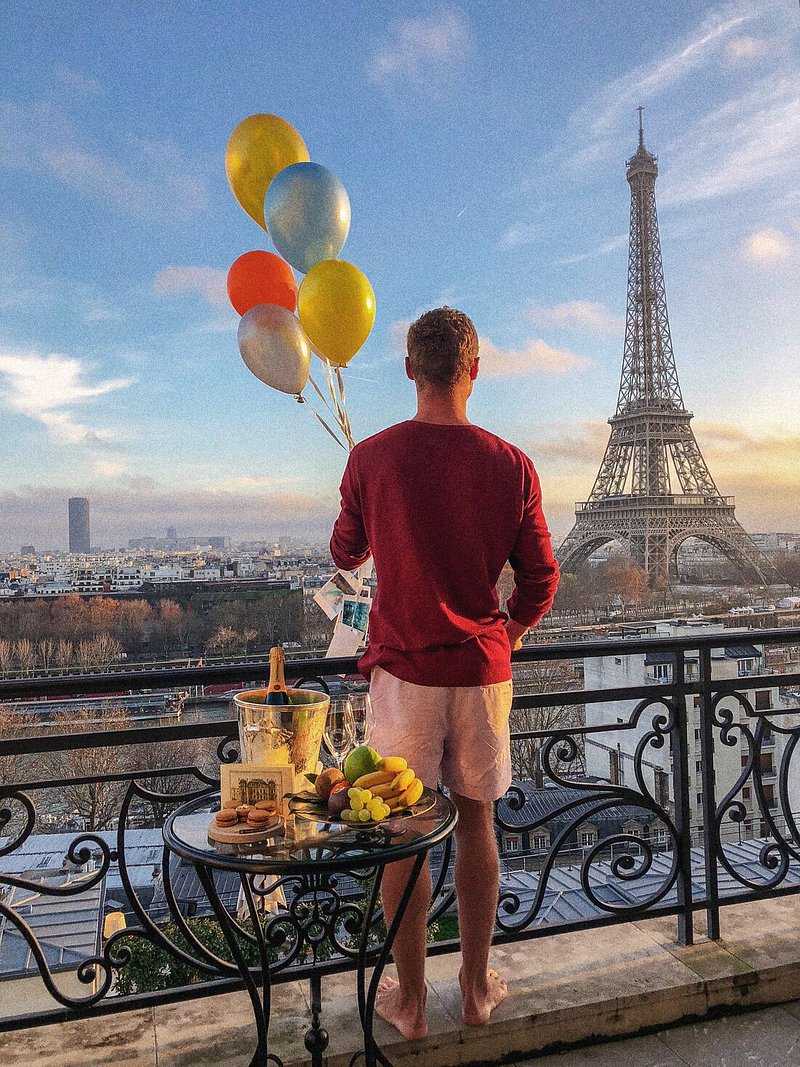Een man die ballonnen vasthoudt op het balkon van Shangri-La Paris met uitzicht op de Eiffeltoren