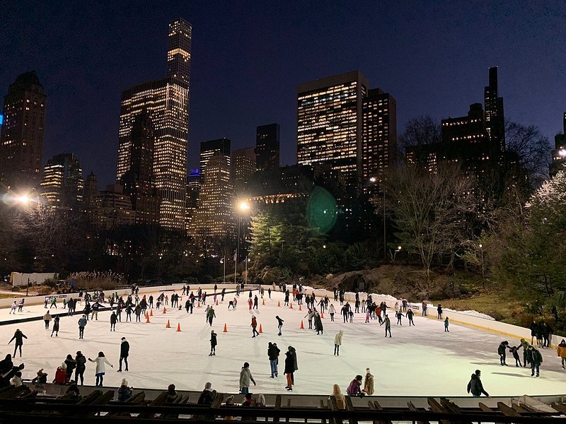 Nighttime skaters enjoy Wollman Rink with the city skyline illuminated in the background