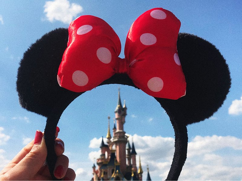 A girl holding up a Mickey Mouse headband against the Disneyland Castle in Paris