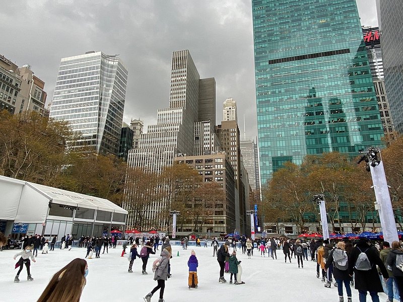 Dozens of ice skaters enjoy Bryant Park ice skating rink with New York skyscrapers in the background