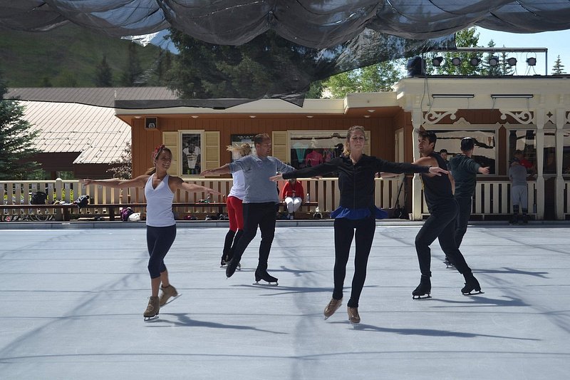 Professional ice skaters hold their arms parallel to the ground as they practice under netting outside