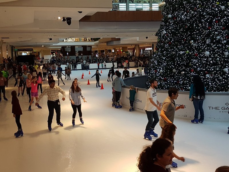 A crowd of people skate around a large indoor Christmas tree inside Galleria Mall