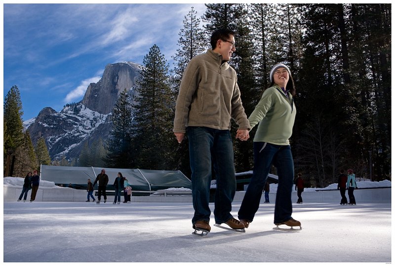 Two skaters hold hands on the Curry Village ice rink, with a view of Half Dome in the background