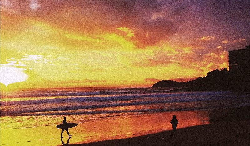 A man with a surfboard walking along Bondi Beach at sunset