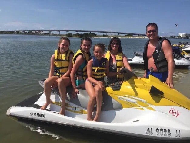 Family sitting on and standing around jet ski