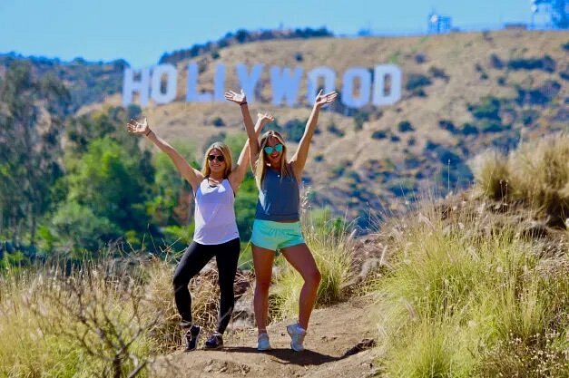 Two people standing with their hands up in front of Hollywood Sign