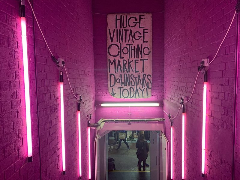 Neon lights surrounding a sign that says huge vintage clothing market downstairs today