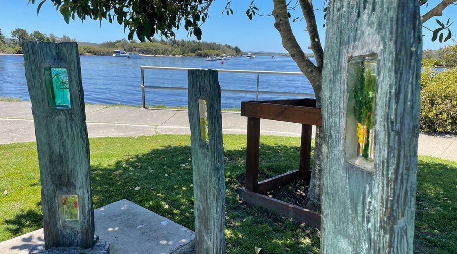 'Windows in Wood' is by local artist Bronwyn Fife, is one of the artworks along the the Myall Riverside Art Walk. It uses 3 bronzed historic turpentine fence posts to symbolise the towns' past. They are inset with glass images of local flowers.