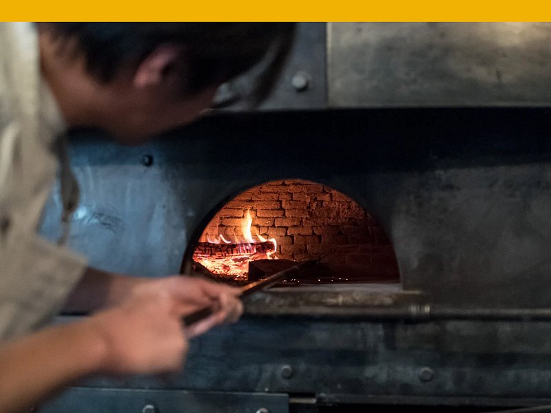 Chef no Seirinkan a colocar uma piza num forno de piza em tijolo.
