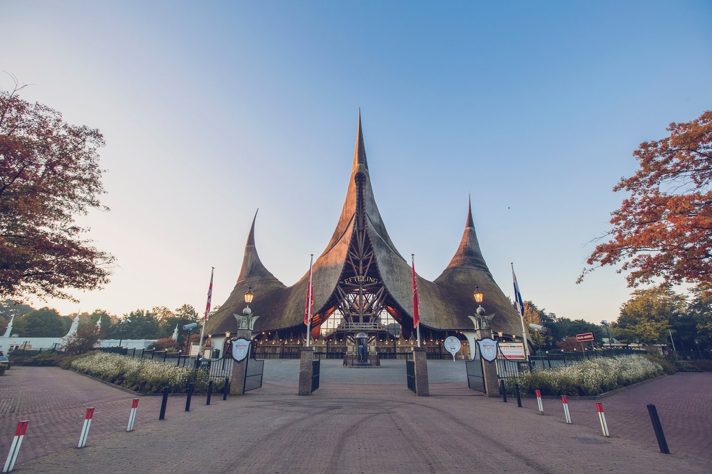 Entrance of a theme park with pointed, thatched roof structures and flags.